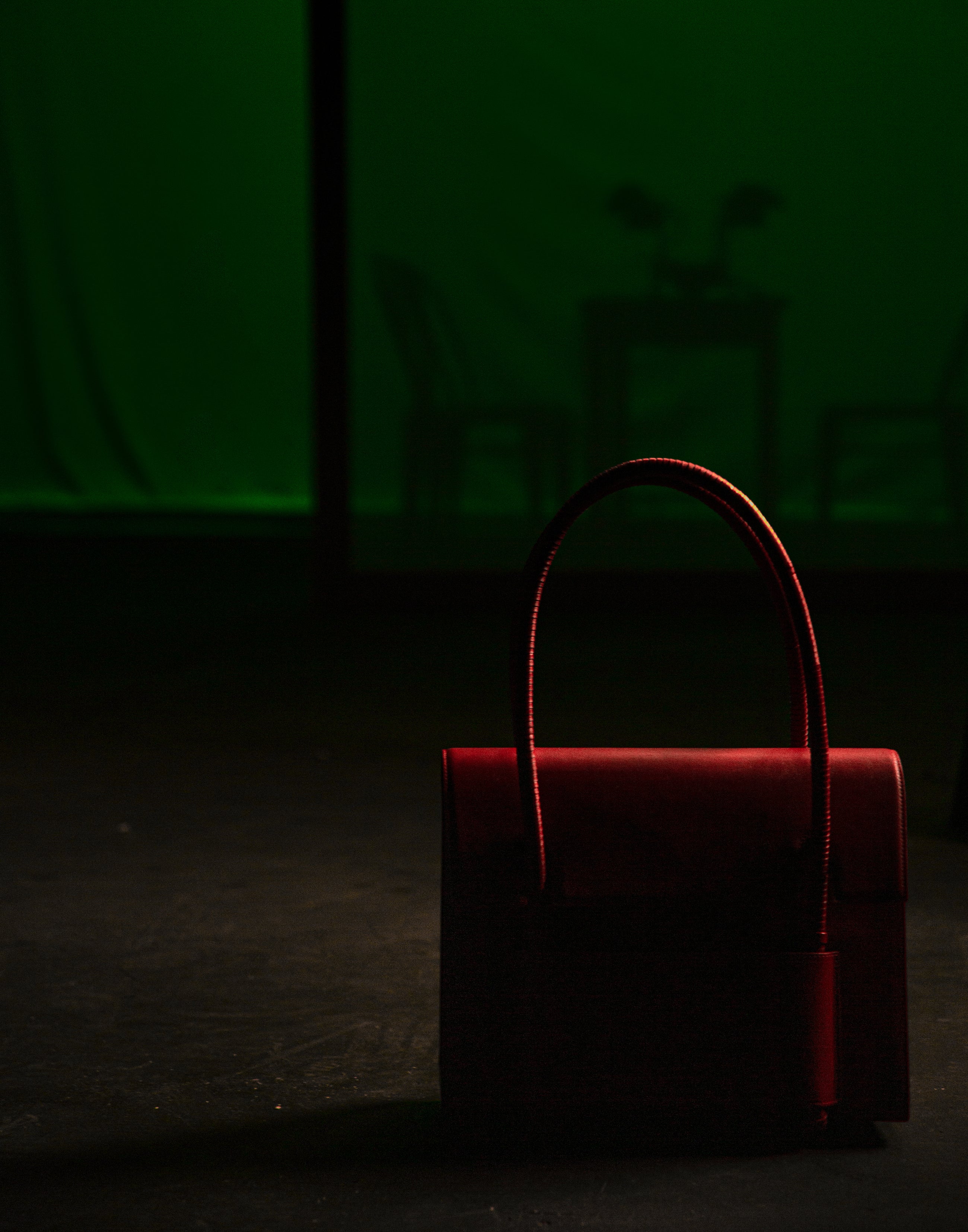 KUN HONG CHUA MOTHER SATCHEL Red handbag in a dark setting with a green screen background KUN HONG CHUA MOTHER SATCHEL in HÓNG (2022) by Xiao Han and Kun Hong