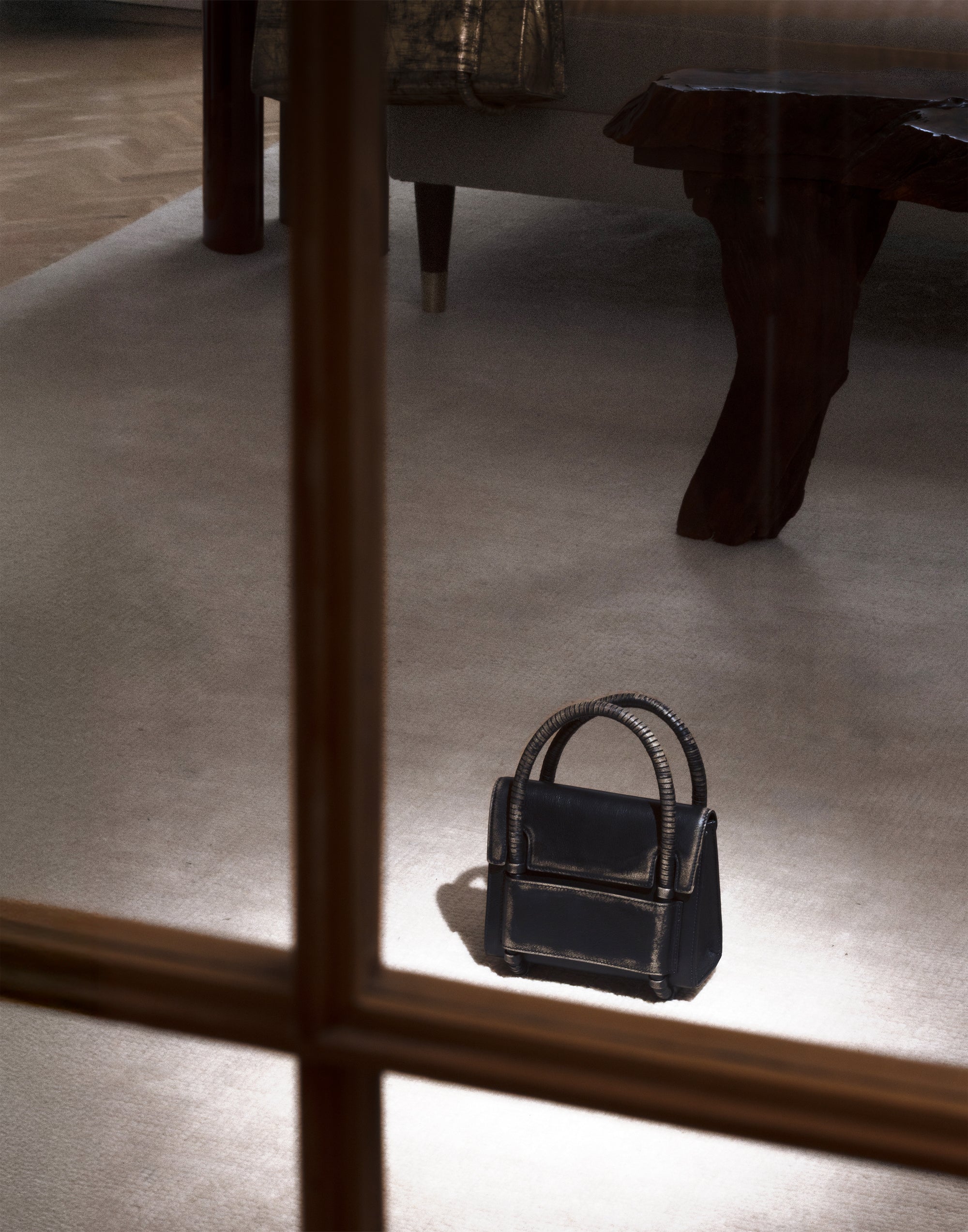 KUN HONG CHUA BAG Black handbag on a reflective surface with a blurred indoor setting