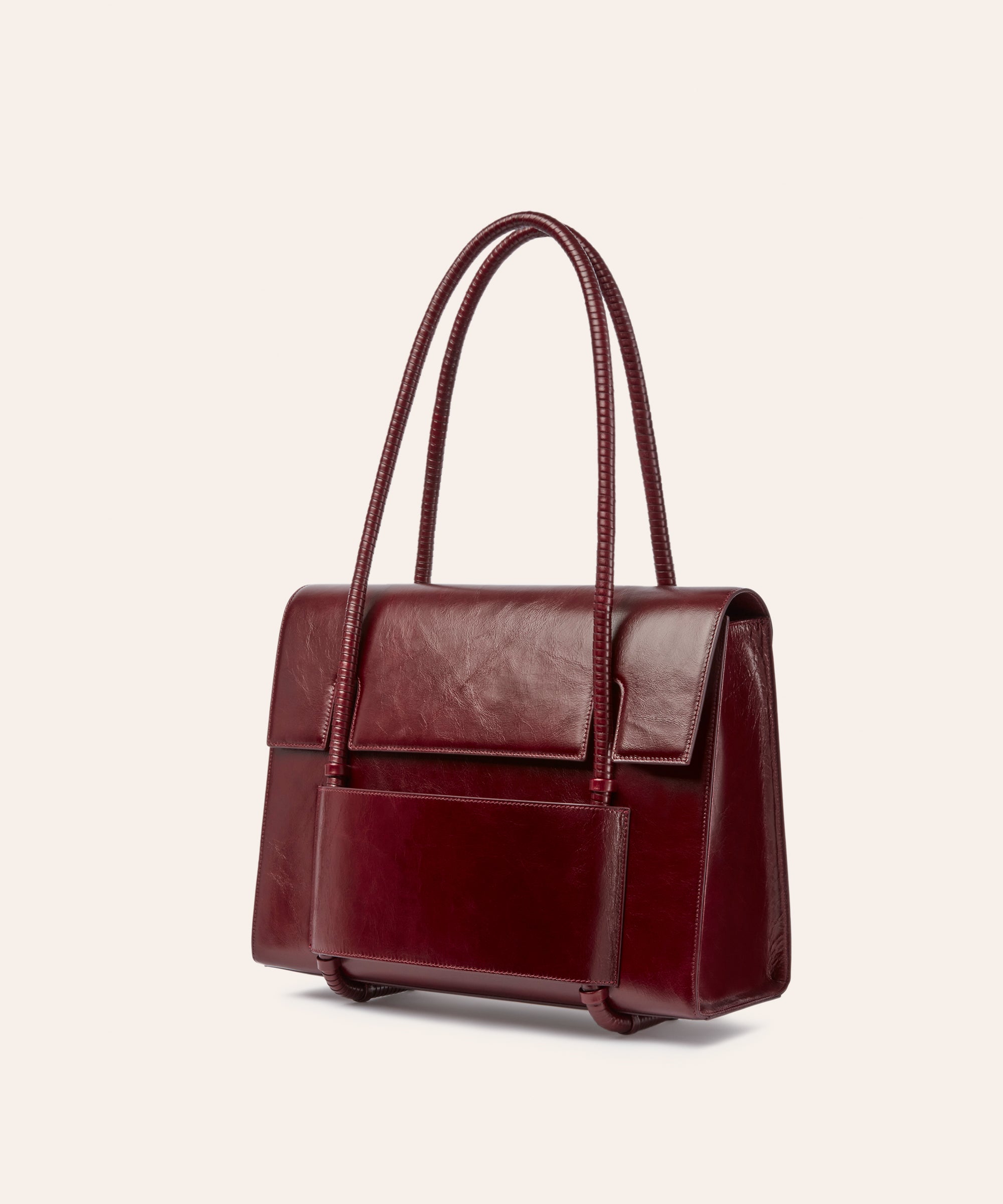 KUN HONG MOTHER SATCHEL LACQUER RED KUN HONG MOTHER SATCHEL Maroon handbag with leather wrapped double handle on a beige background