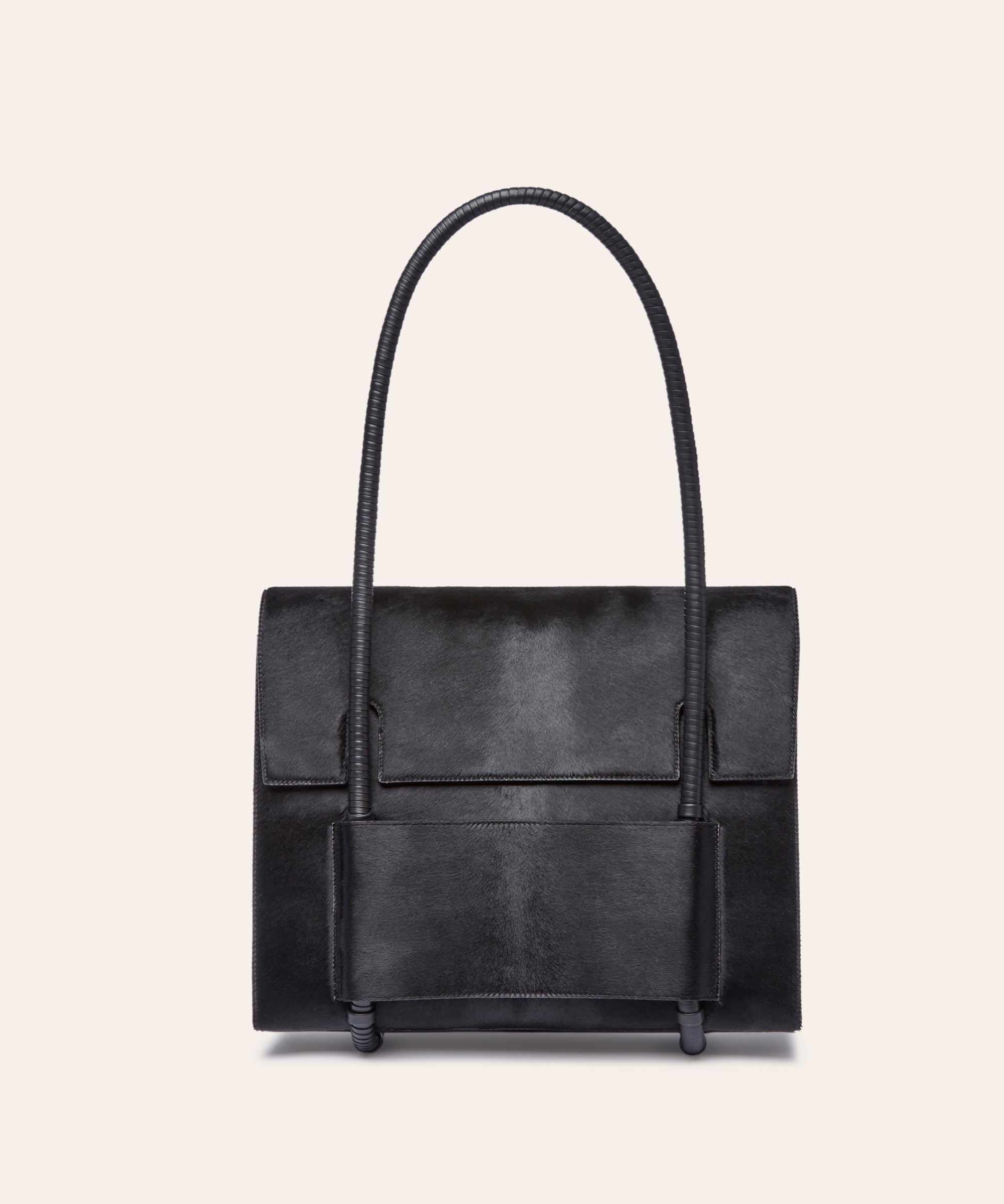 KUN HONG Mother Satchel in Black Fuzz, Black handbag with a unique handle design on a beige background