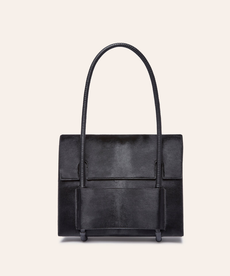 KUN HONG Mother Satchel in Black Fuzz, Black handbag with a unique handle design on a beige background