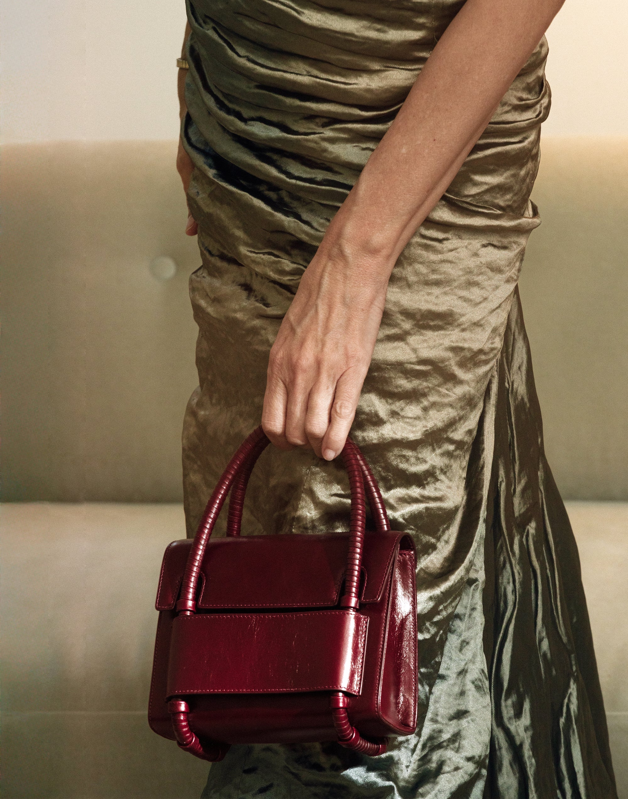 KUN HONG CHUA BAG Person holding a burgundy KUN HONG CHUA DAUGHTER IN LACQUER RED handbag wearing a metallic dress.