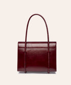KUN HONG MOTHER SATCHEL LACQUER RED Maroon handbag with leather wrapped double handle on a beige background