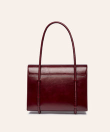 KUN HONG MOTHER SATCHEL LACQUER RED Maroon handbag with leather wrapped double handle on a beige background